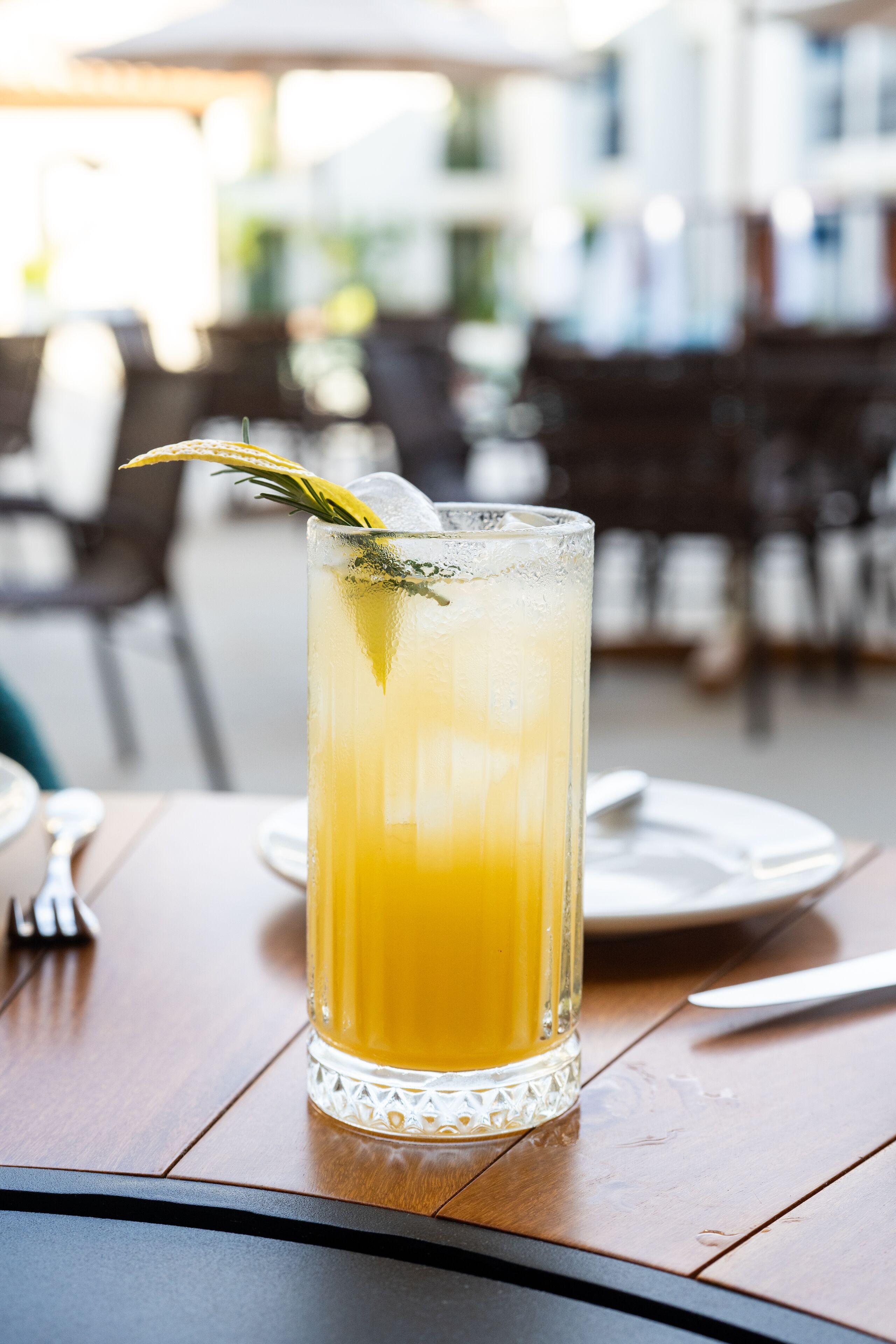 Un vaso alto de jugo de naranja con una ramita de romero sobre una mesa de madera.