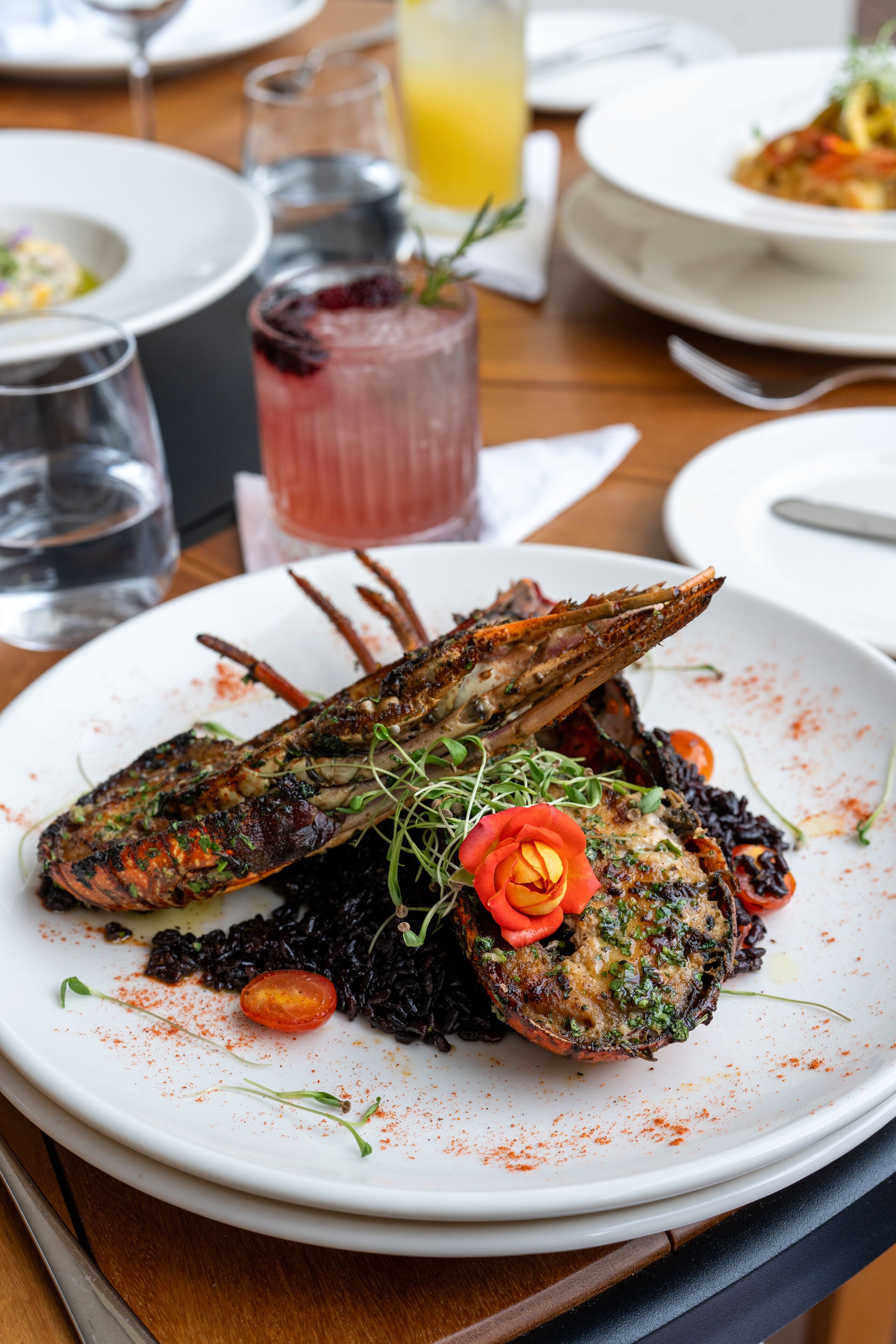 A seafood dish on a white plate with a glass of red beverage and a water glass in the background.