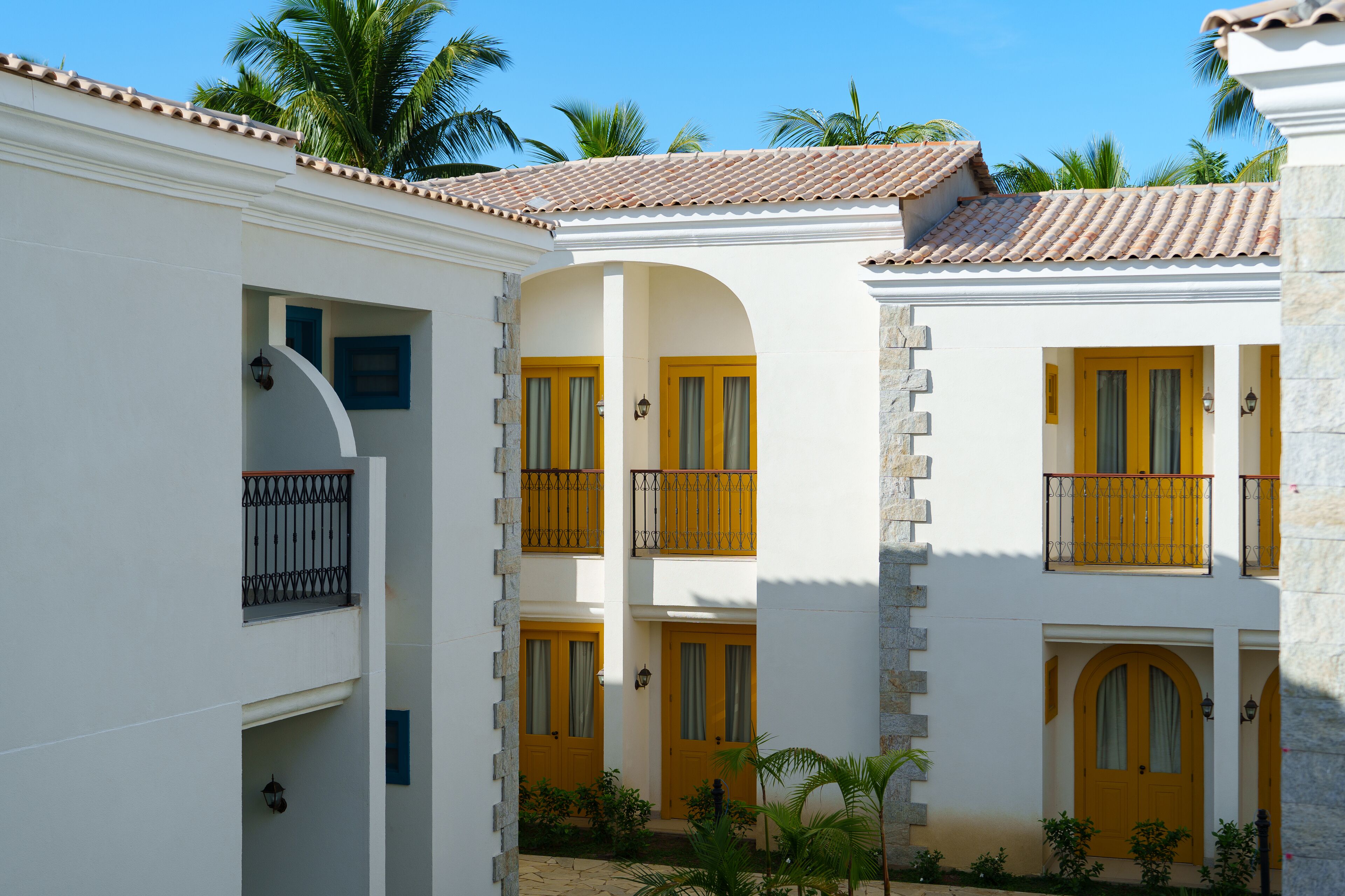 A courtyard with white buildings, yellow doors, and stone pillars.