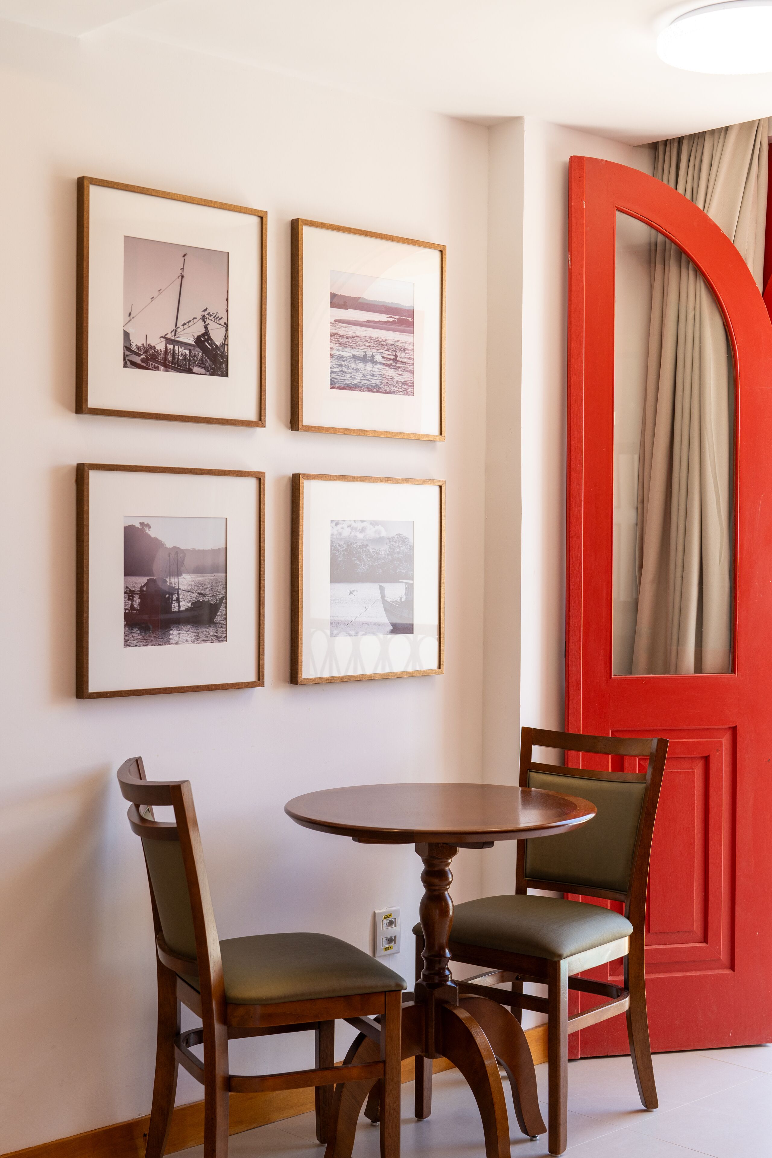 A dining area with a round table and four chairs, a red door, and four framed photographs on the wall.
