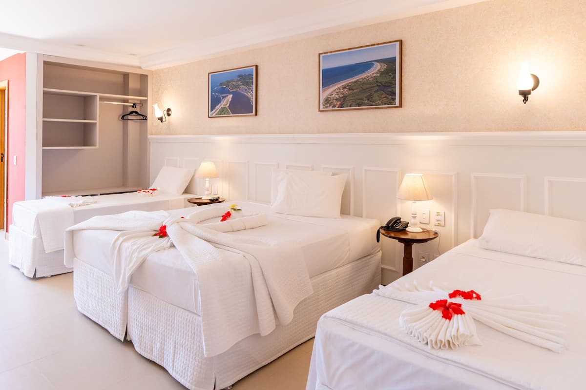 A hotel room with three beds, a bedside table with a lamp, a wall-mounted picture, and a wardrobe.