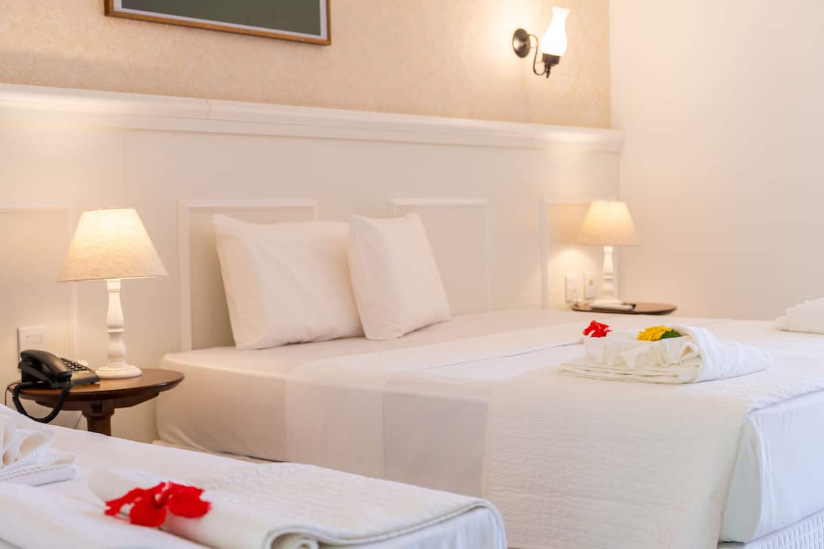 A hotel room with two beds, white linens, a bedside table with a lamp, a phone, and a towel with flowers.