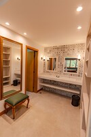 Un baño con tocador, un espejo grande, una banca y azulejos con diseño.