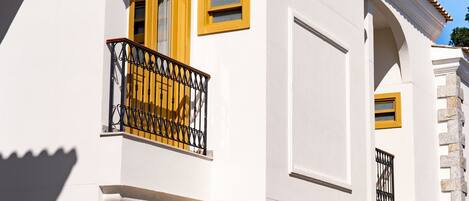 A white building with yellow accents, including a door, windows, and balcony railings.