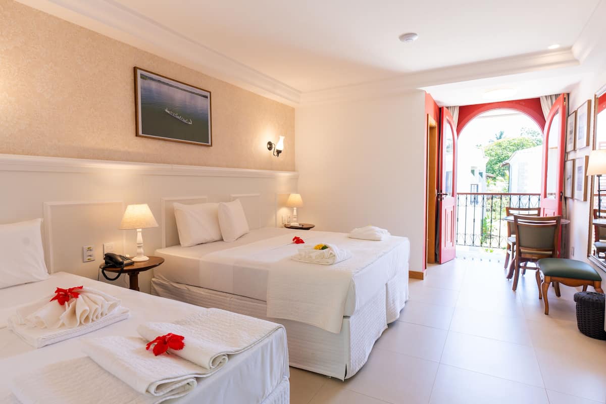 A hotel room with two beds, a balcony, and a dining area.