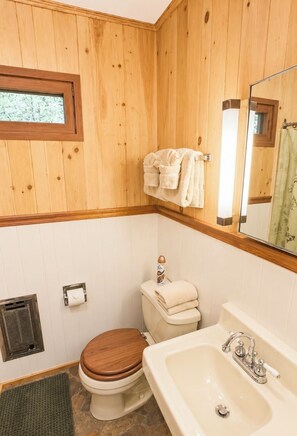 Ein Badezimmer mit Holzwänden, einer Toilette, einem Waschbecken und einem Fenster.