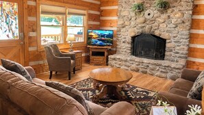 A cozy log cabin interior with a stone fireplace, wooden furniture, and a television. - 4 Br-Minutes to National Park!Enjoy the Farm Life! (Cosby)