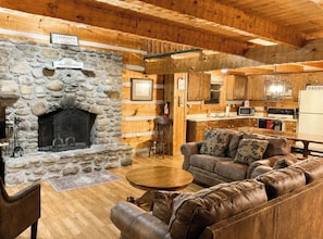 A rustic interior with a stone fireplace, wooden walls, a leather sofa, and a kitchen area.
