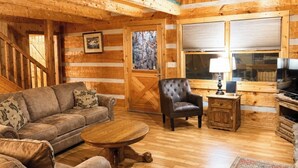 A log cabin interior with a sofa, armchair, coffee table, TV, and wooden cabinets. - 4 Br-Minutes to National Park!Enjoy the Farm Life! (Cosby)