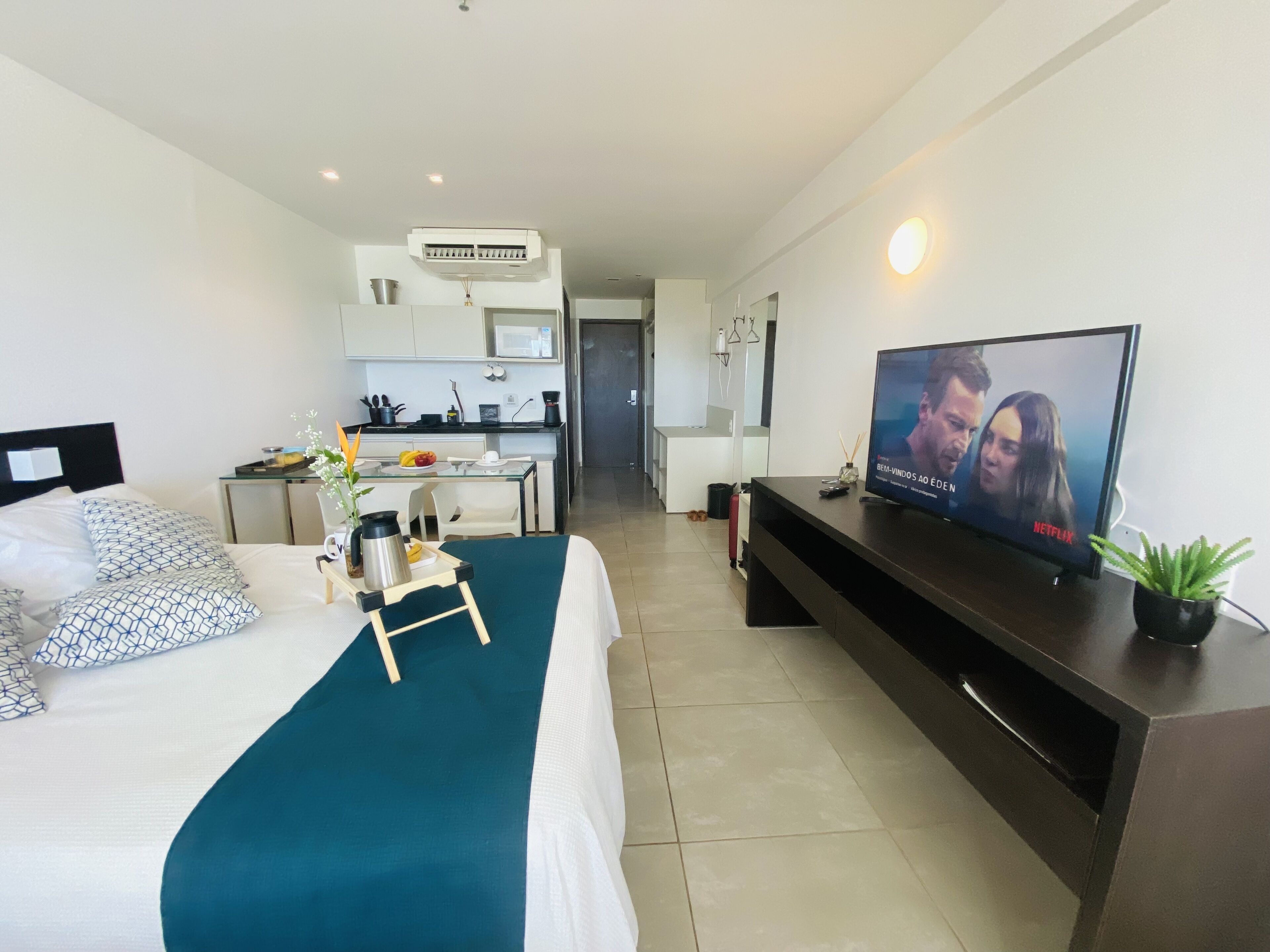 Una habitación de hotel moderna con cama, televisor, kitchenette pequeño y zona de comedor.