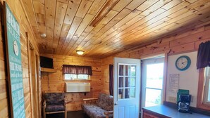 A wooden cabin interior with a dining table, two chairs, a sofa, a kitchen area, and a door leading outside. - East Crooked Lake Front Cabin 2 (Nevis)
