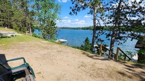 A lakeside deck with a wooden walkway, green chairs, and a view of the lake. - East Crooked Lake Front Cabin 2 (Nevis)