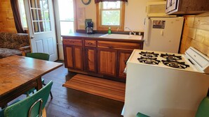 A wooden cabin interior with a kitchen area featuring a stove, sink, and cabinets. - East Crooked Lake Front Cabin 2 (Nevis)