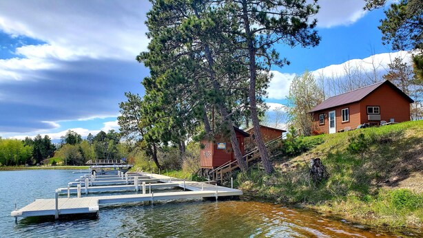 A lakeside cabin with a dock extending into the water, surrounded by trees and a clear sky. - East Crooked Lake Front Cabin 2 (Nevis)