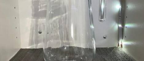 A clear glass pitcher on a shelf with a textured mat labeled "PITCHER".