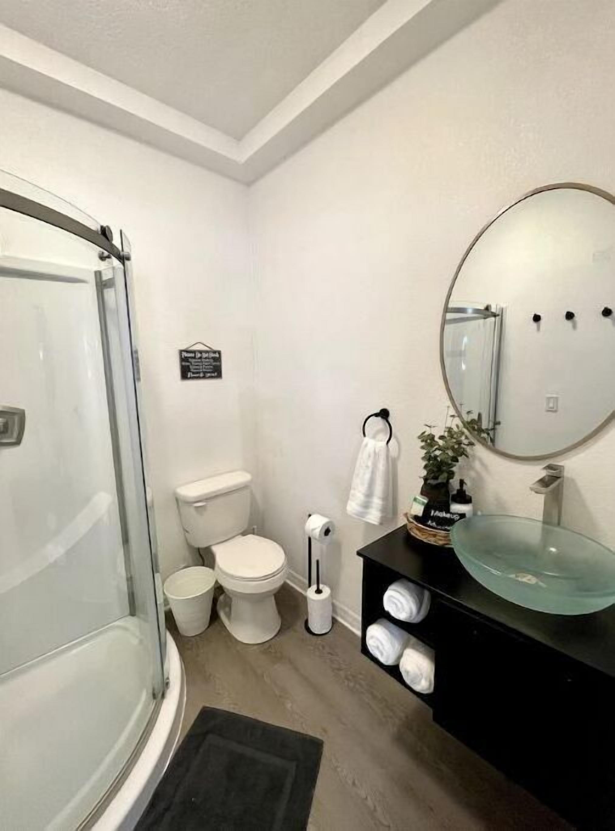 A modern bathroom with a glass shower enclosure, a toilet, a bidet, and a black vanity with a glass sink.