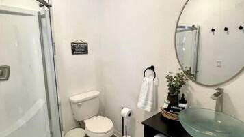 A modern bathroom with a glass shower enclosure, a toilet, a bidet, and a black vanity with a glass sink.
