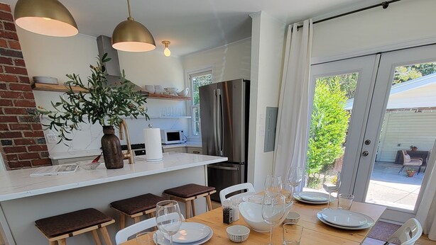 Una cocina moderna con una mesa de madera para cuatro personas, sillas blancas y un amplio ventanal con vistas a un jardín.