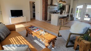 Una sala moderna con una mesa de centro de madera, un sofá y un televisor. Cuenta con una zona de cocina con una pared de ladrillo y un comedor con mesa y sillas.