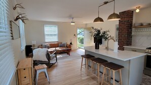 Amplia sala de estar con un sofá grande, piso de madera y una cocina con pared de ladrillo y electrodomésticos modernos.