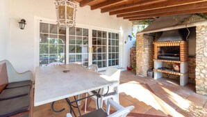 An outdoor patio with a stone oven, white chairs, a table, and a hanging light fixture. - Casa da Saudade - Heated swimming pool, walking distance to town and beach (Carvoeiro)