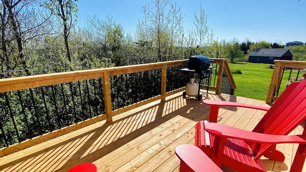 Eine Holzterrasse mit roten Stühlen, einem Grill und einem Wagen mit Propangasflaschen.