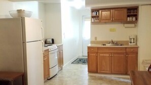 A compact kitchen with a refrigerator, stove, and wooden cabinets. There is a dining area with a table and benches. - 2 Bedroom Railroad layout (Cooperstown)