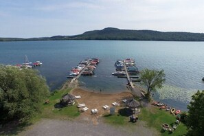 A lakeside marina with boats docked, a sandy beach area, and a small pavilion.