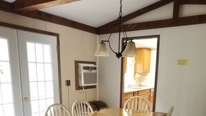 Ein Esszimmer mit Holztisch und weißen Stühlen, einem Deckenventilator und einer durch eine offene Tür einsehbarer Küche.