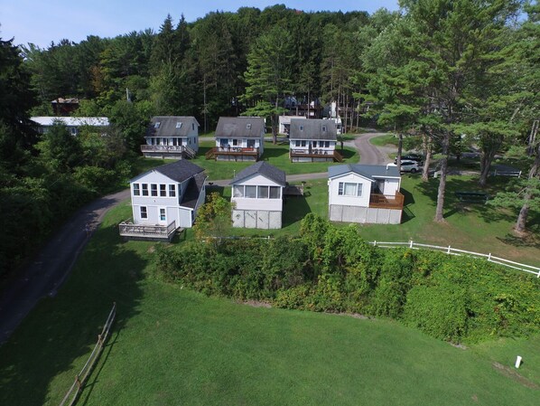 A cluster of cabins with attached decks, surrounded by dense forest and a winding road.