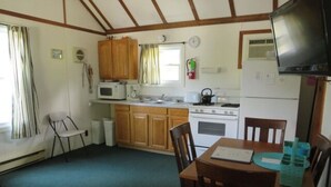 A compact kitchen with wooden cabinets, a microwave, a stove, and a dining table with chairs.