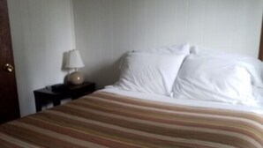 A bed with a striped bedspread, a bedside lamp, and a painting on the wall.