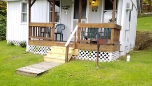 A small, single-story cabin with a porch, a wooden deck, and a small ramp leading to the entrance.