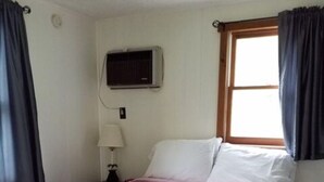 A single bed with a floral-patterned bedspread, a nightstand with a lamp, and a window with curtains.