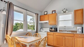A kitchen with wooden cabinets, a white stove, a microwave, and a sink. There are two windows with curtains, a table with chairs, and a view of trees outside. - 3 Bedroom Cottage only 10 minutes from Cooperstown (Cooperstown)
