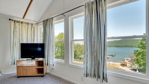 Et værelse med et stort vindue, et fladskærms-tv på et træstel og udsigt til en sø og en ankomstbro.