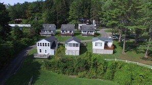 A cluster of cabins with attached decks, surrounded by dense forest and a winding road.