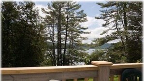 A wooden deck with a white chair, overlooking a forested area and a body of water.