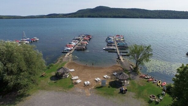 A lakeside marina with boats docked, a sandy beach area, and a small pavilion.
