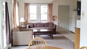 A living room with a sofa, a dining table with chairs, and a kitchen area in the background.
