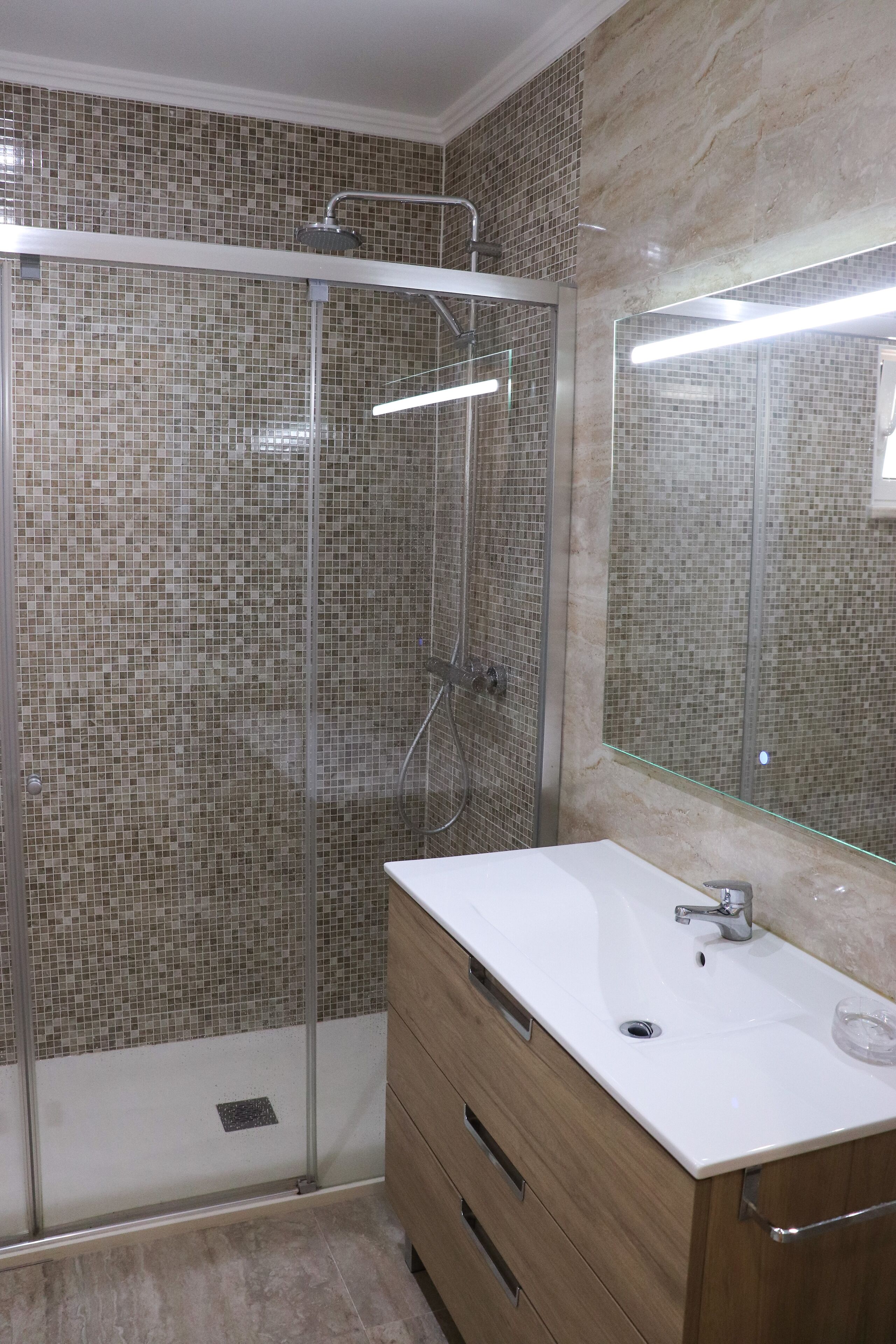 Ein Badezimmer mit einer Duschkabine, einem weißen Waschbecken und einem Holzausziehtisch.