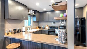 Une cuisine moderne avec des meubles de couleur sombre, un grand îlot central doté de tabourets et une pancarte « BIENVENUE » au-dessus de la porte.