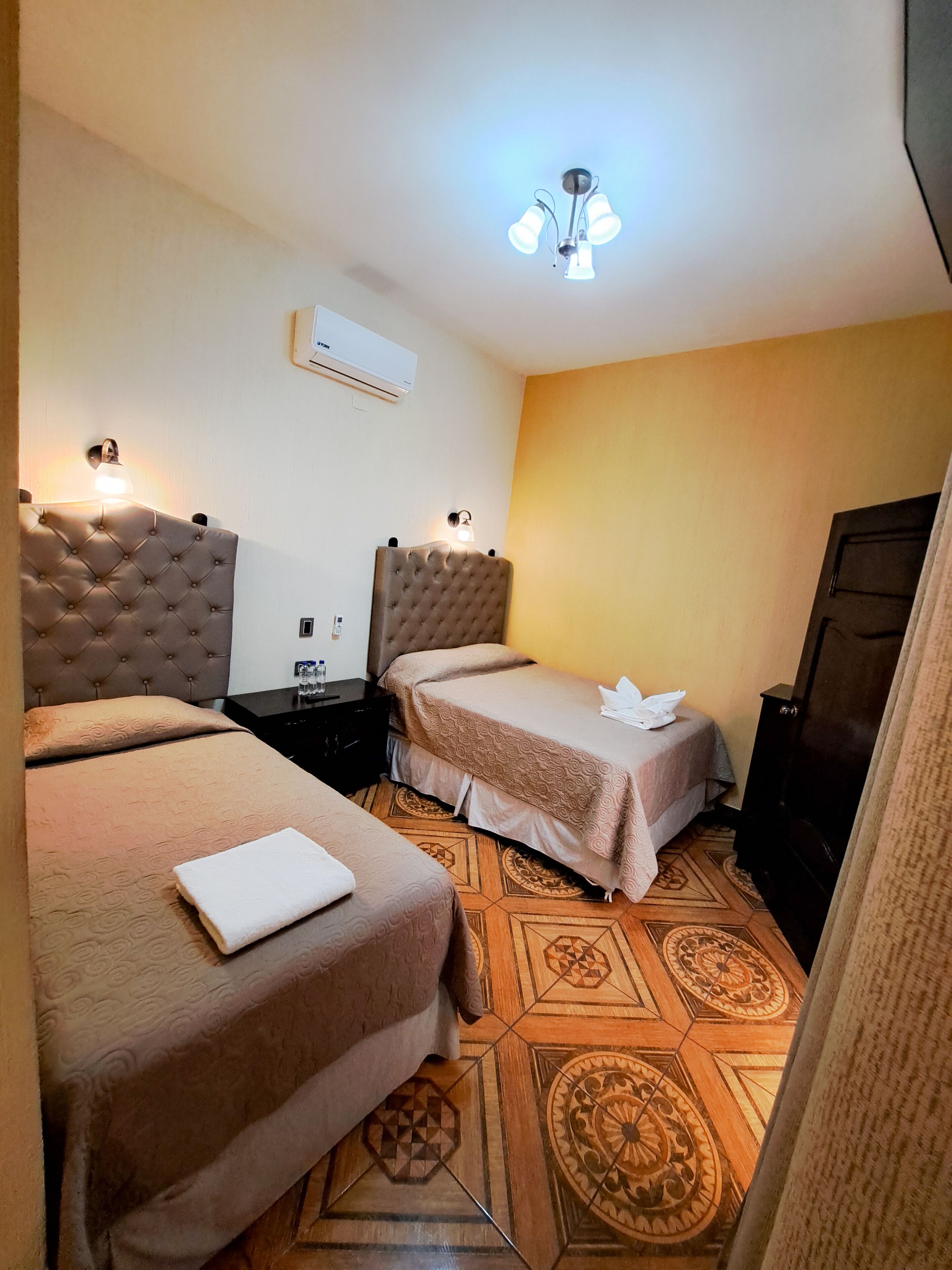 A hotel room with two beds, a ceiling fan, an air conditioner, and a patterned floor.