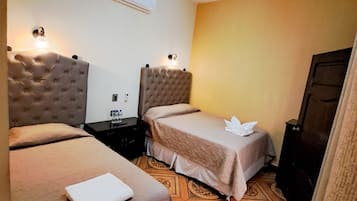 A hotel room with two beds, a ceiling fan, an air conditioner, and a patterned floor.