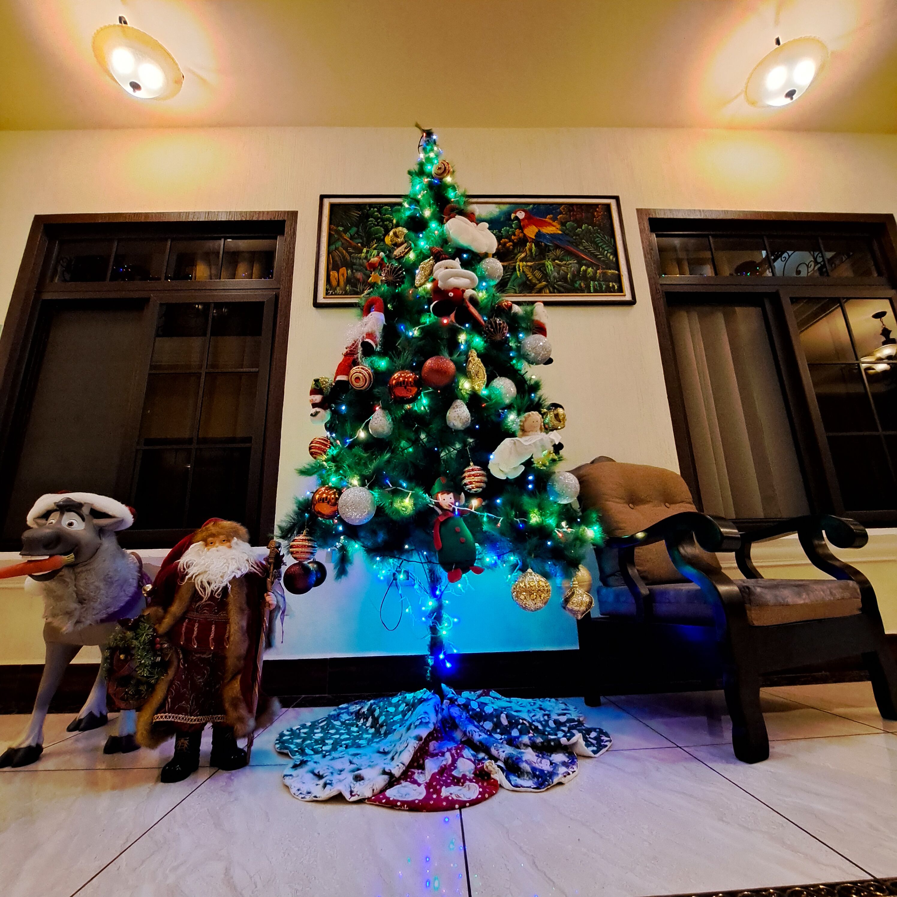 Árvore de Natal decorada com enfeites e luzes, um brinquedo de pelúcia e um cobertor no chão.
