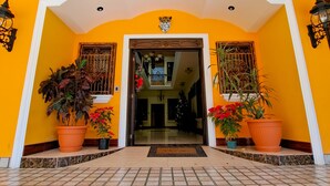 L’entrée d’un hôtel, avec un sol carrelé, une arche centrale et des plantes en pot de chaque côté.