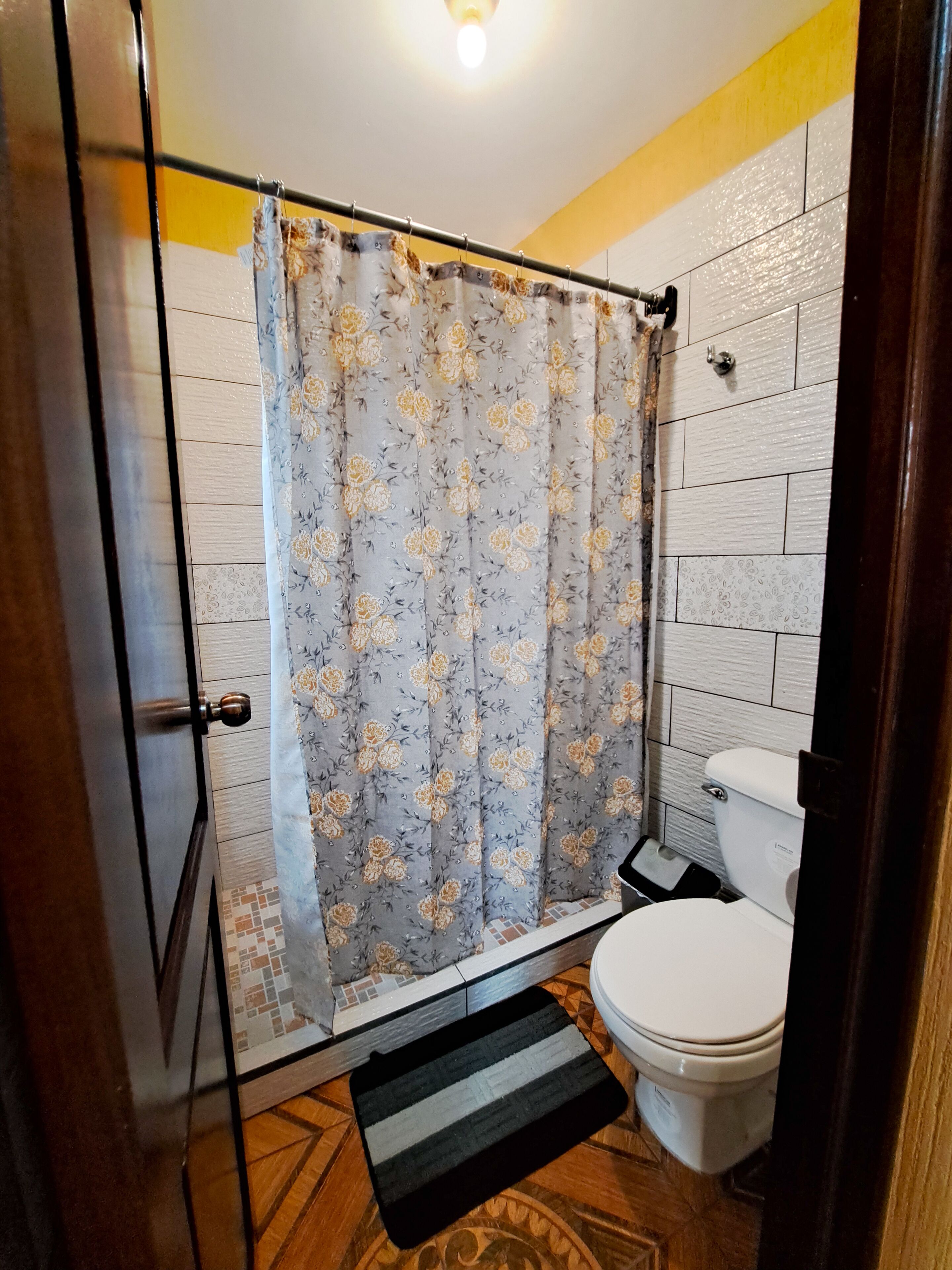 Un baño con cortina de ducha, inodoro y suelo de madera.