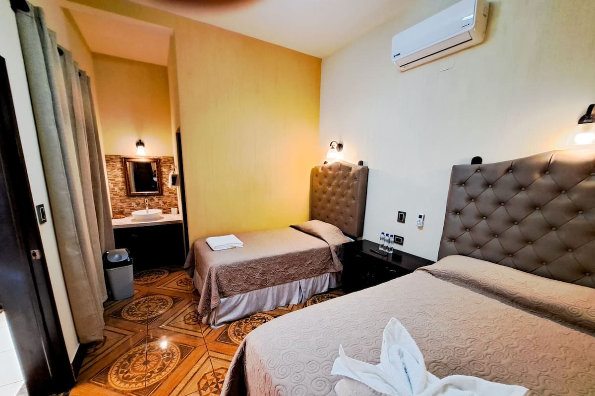 Habitación de hotel con dos camas, un baño con lavamanos y piso estampado.