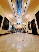 Um hall amplo com piso de mármore polido, uma árvore de Natal e um teto alto com detalhes decorativos.