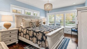 A bedroom with a large bed, bedside lamps, a chandelier, and a view through the window.